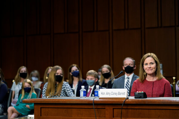 Justice Amy Coney Barrett during her confirmation hearing, with her husband and children behind her. Anti-abortion scholars say her career and family life, as a mother of seven, is an example of how the challenges of balancing work and family are less of an issue.