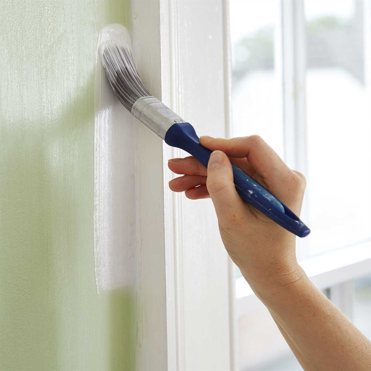 woman edge painting near window trim inside home