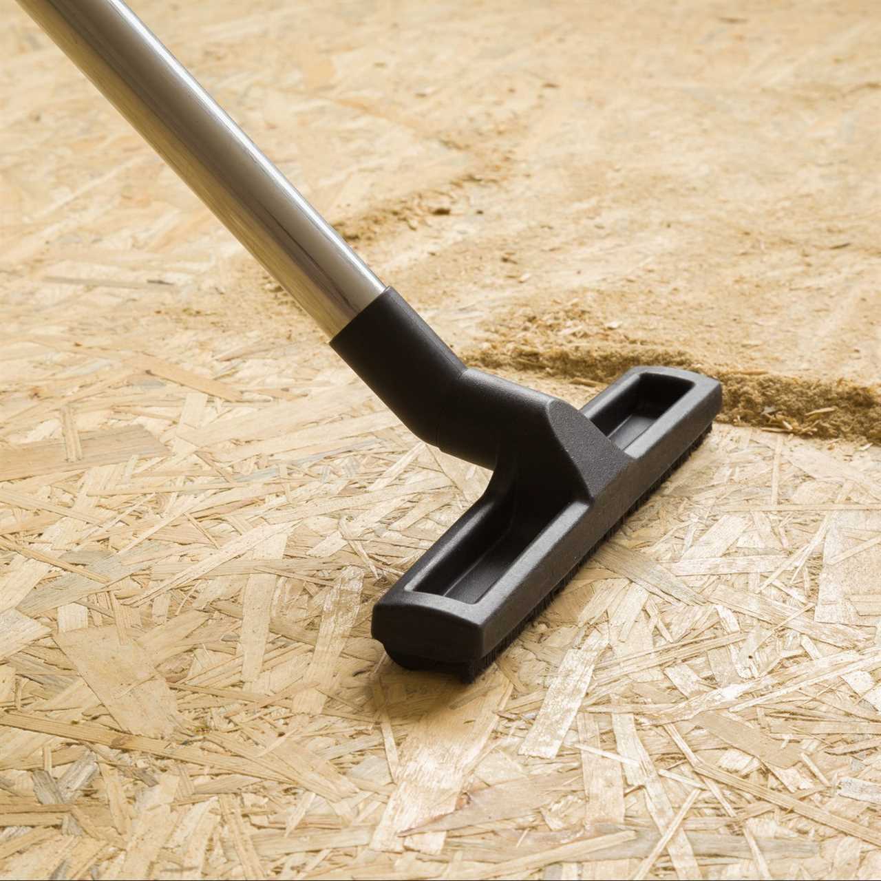 Black nozzle of professional vacuum cleaner vacuuming sawdust from osb board floor. Closeup. Cleaning garbage after repair work.