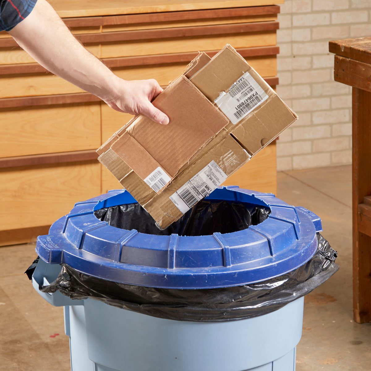 hand putting broken down box through a hole in the lid of a garbage can