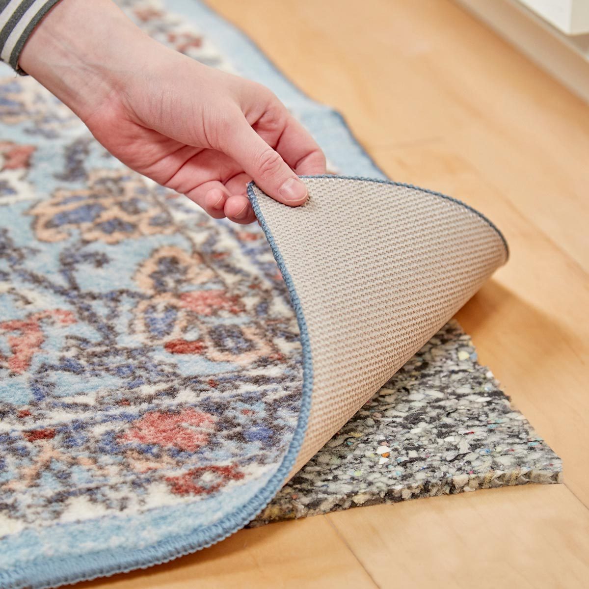 hand lifting the corner of an area rug to reveal carpet padding