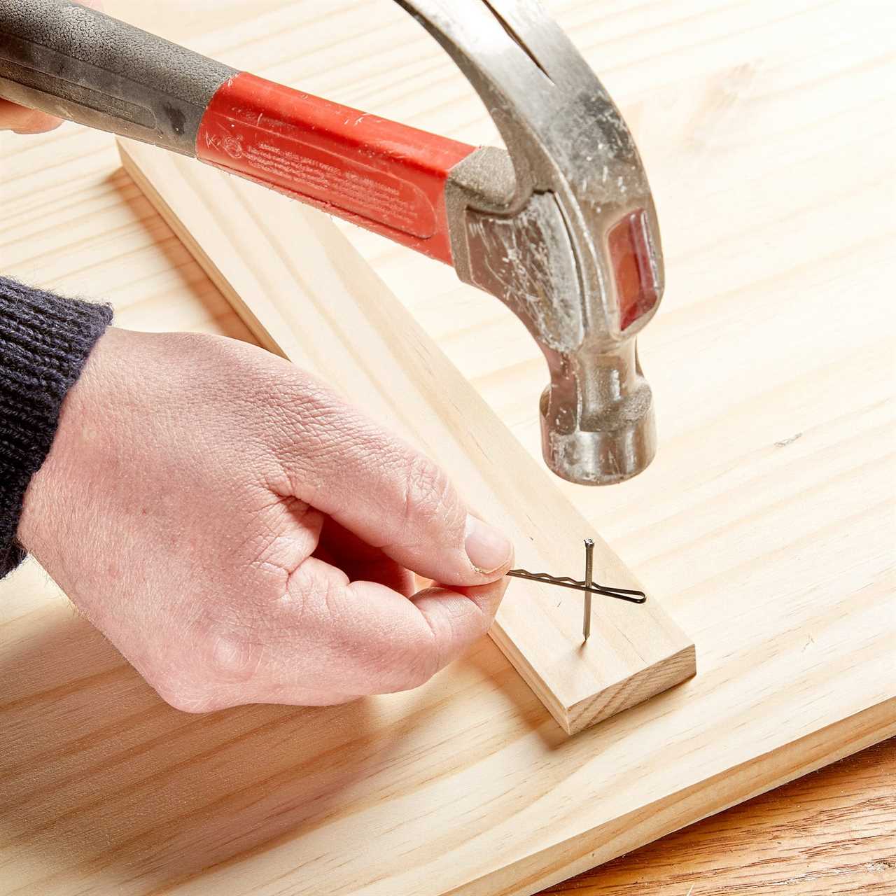 using a poppy pin to hold a nail to safely hammer into a piece of wood