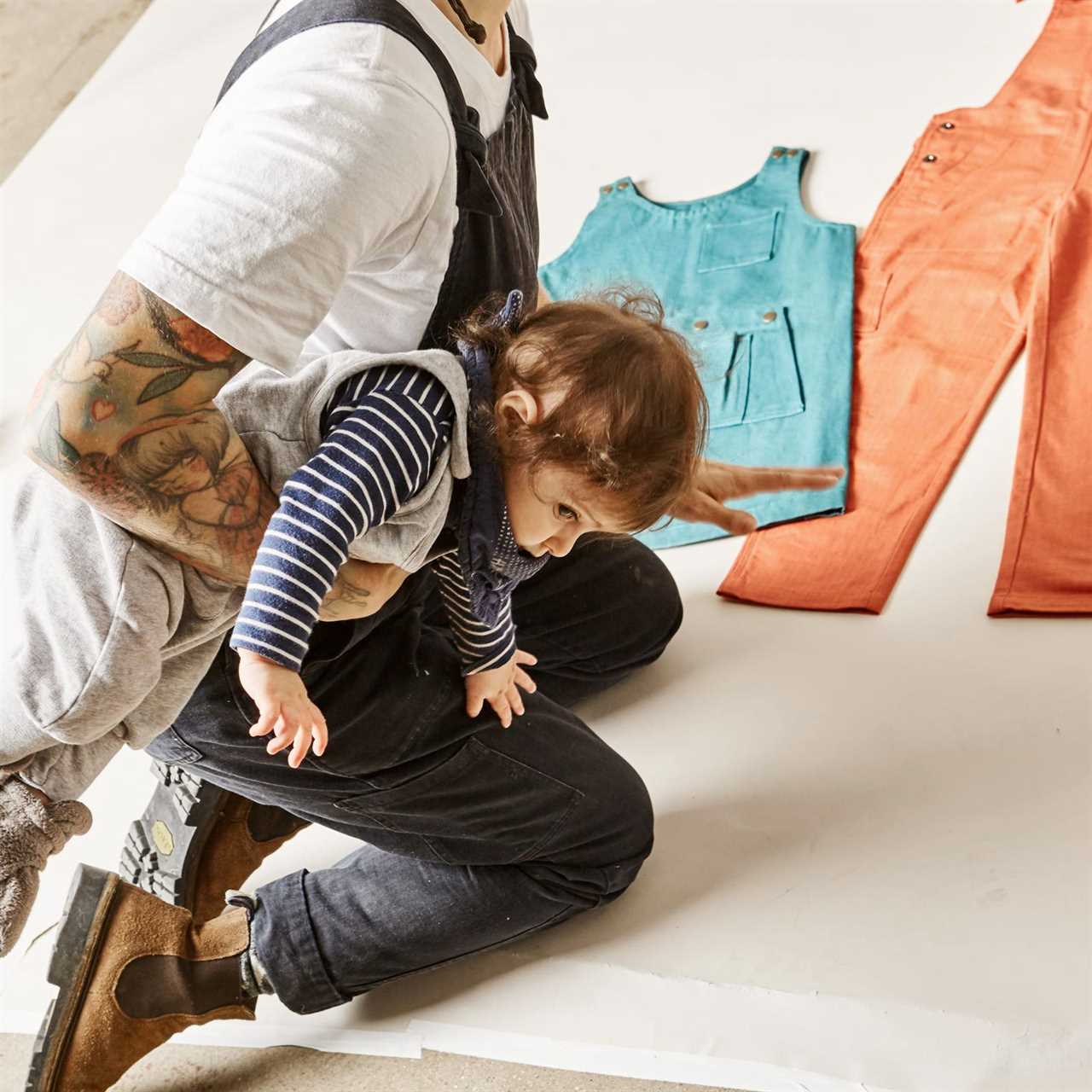 Bella Weinstein kneeling andholding her child while looking at clothing on the ground