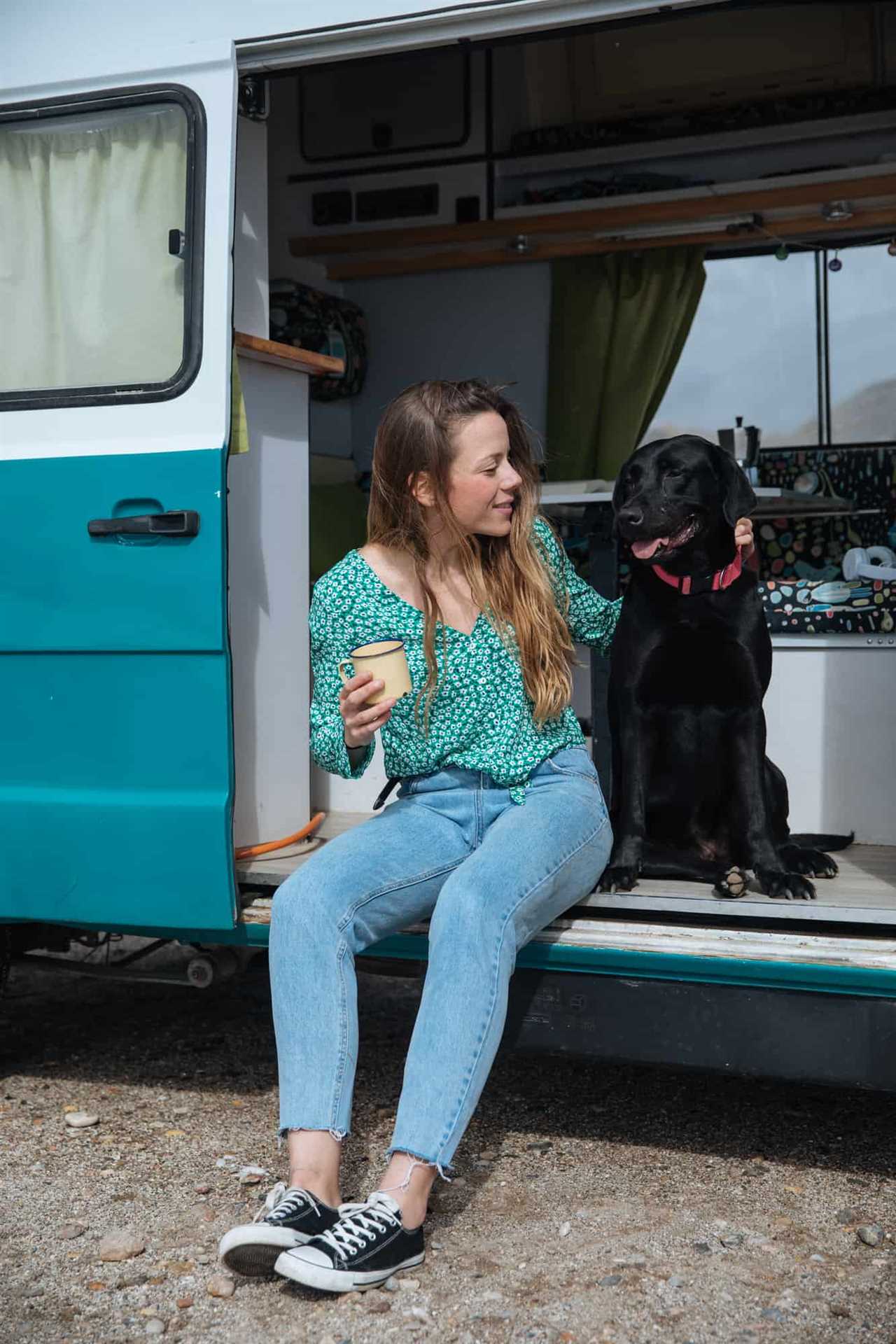 Happy young woman sitting with her black dog in the doorway of a camper van