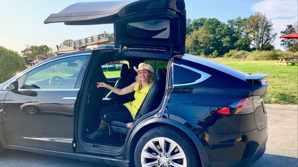 woman sitting at the backsit of a tesla model x with the door wide open