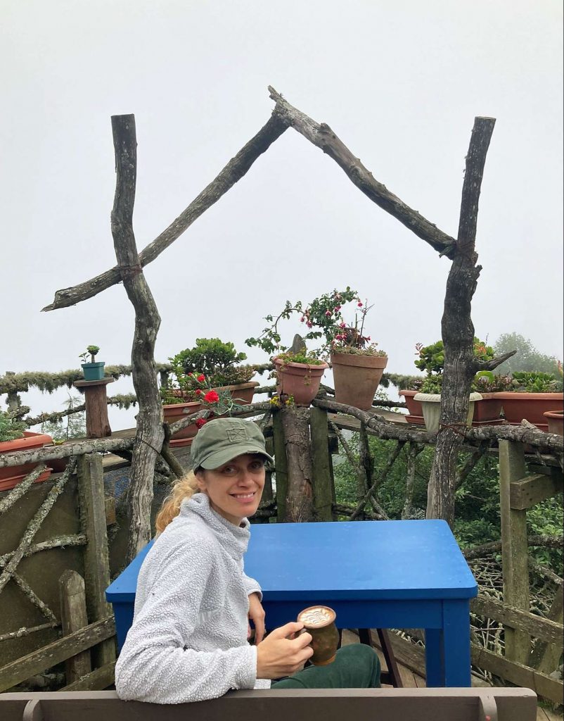 woman sitting on a table holding a drink at hobbitenango