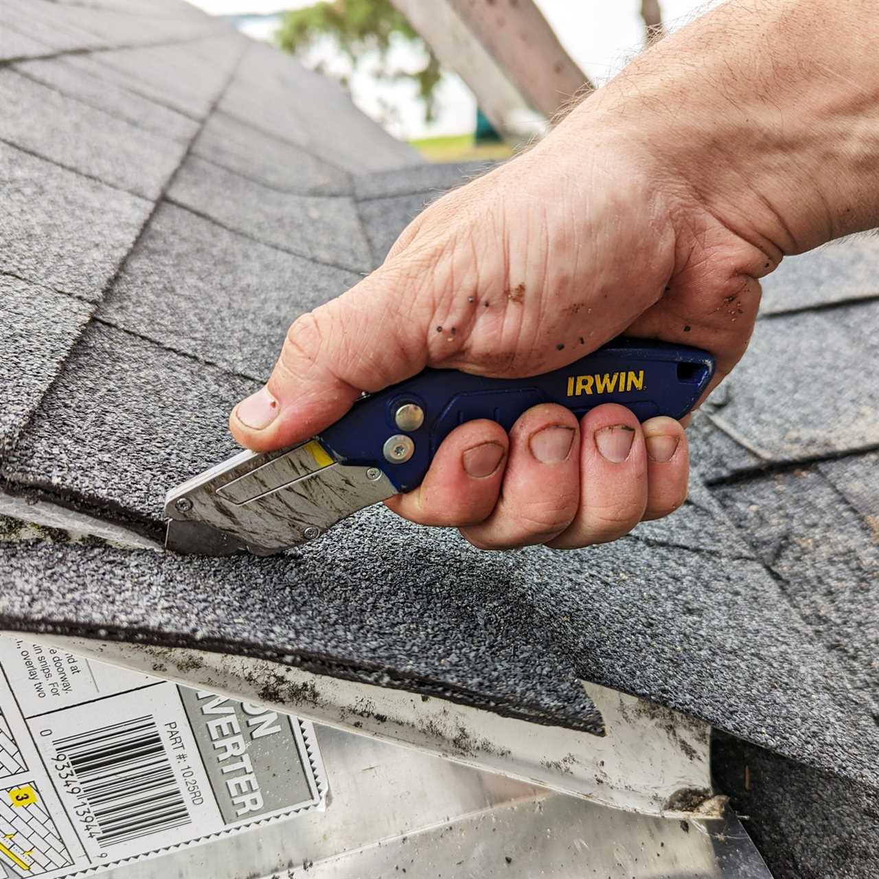 hand using a Irwin Pro Flip Utility Knife to cut roof shingles