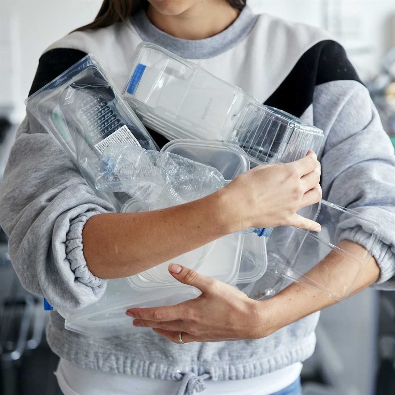 Woman holding armful of used plastic containers in kitchen