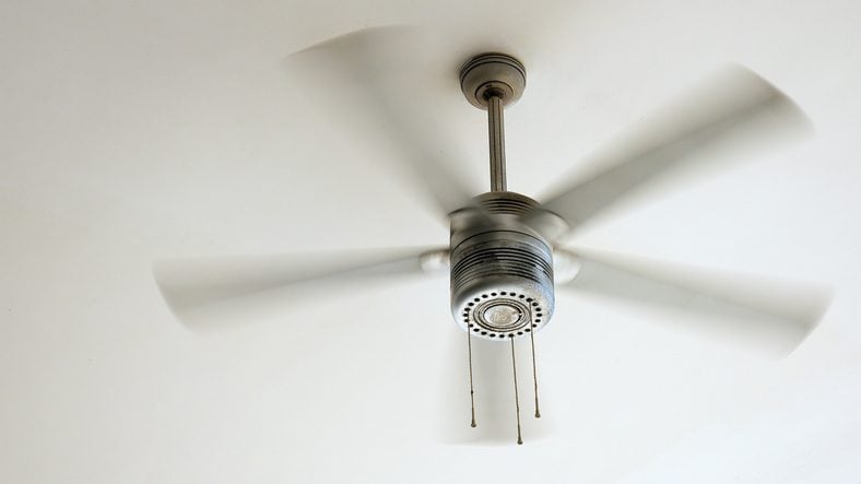 Ceiling fan is rotating at the ceiling of the room. Electric climate equipment.