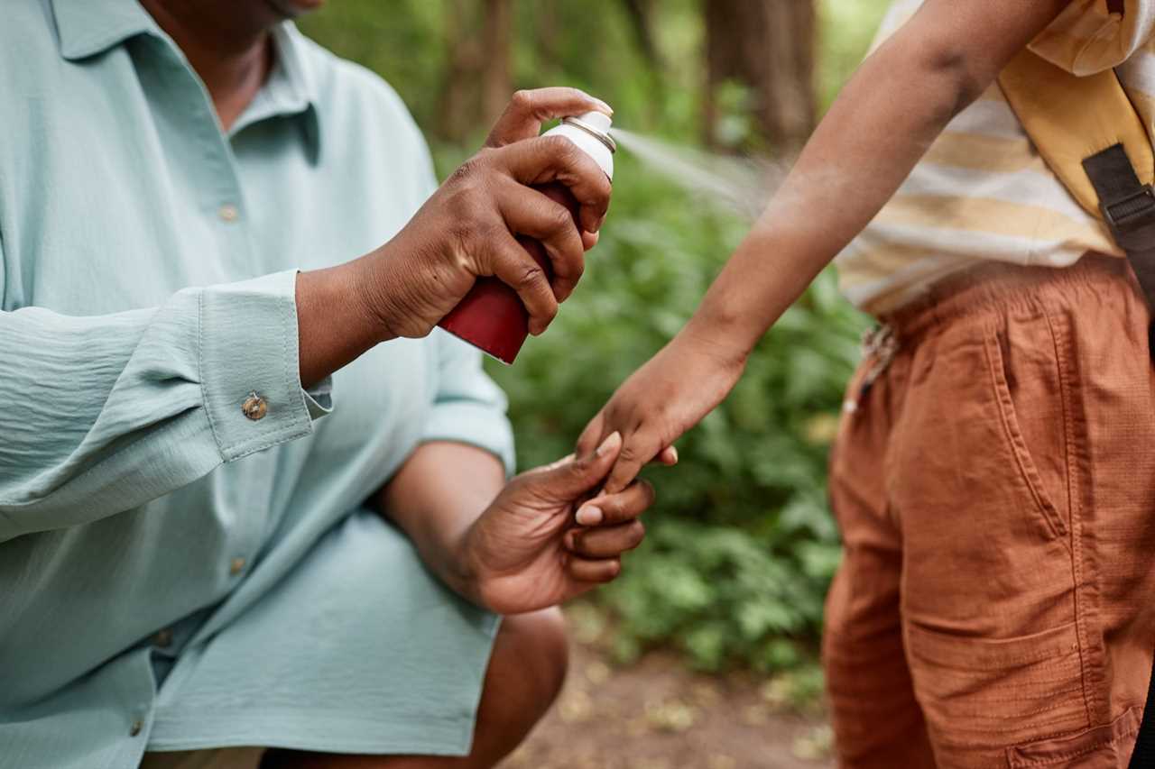 Closeup of caring black mother using baby safe bug repellent for daughter