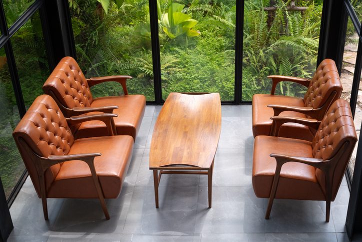 room with a brown sofa and chairs sitting in front of a large window in a wooded area