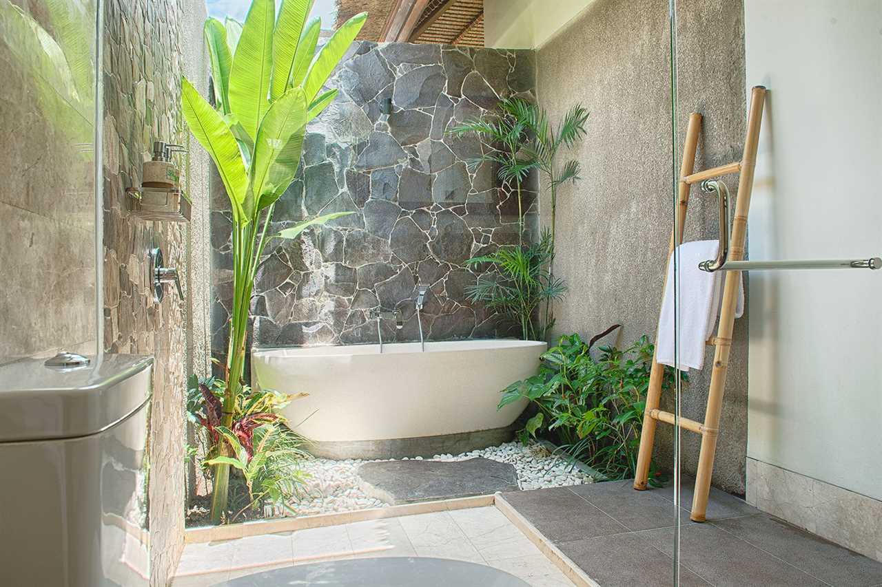 Luxury Interior Tropical Bathroom Of The Dream with a Bathtub and open ceiling, tropical plants and gravel surround the tub with the toilet and showerr glass in the foreground