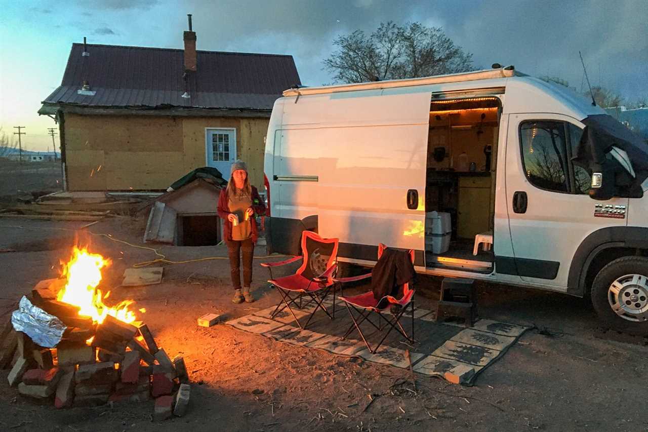 A woman next to a campfire in front of a white van.